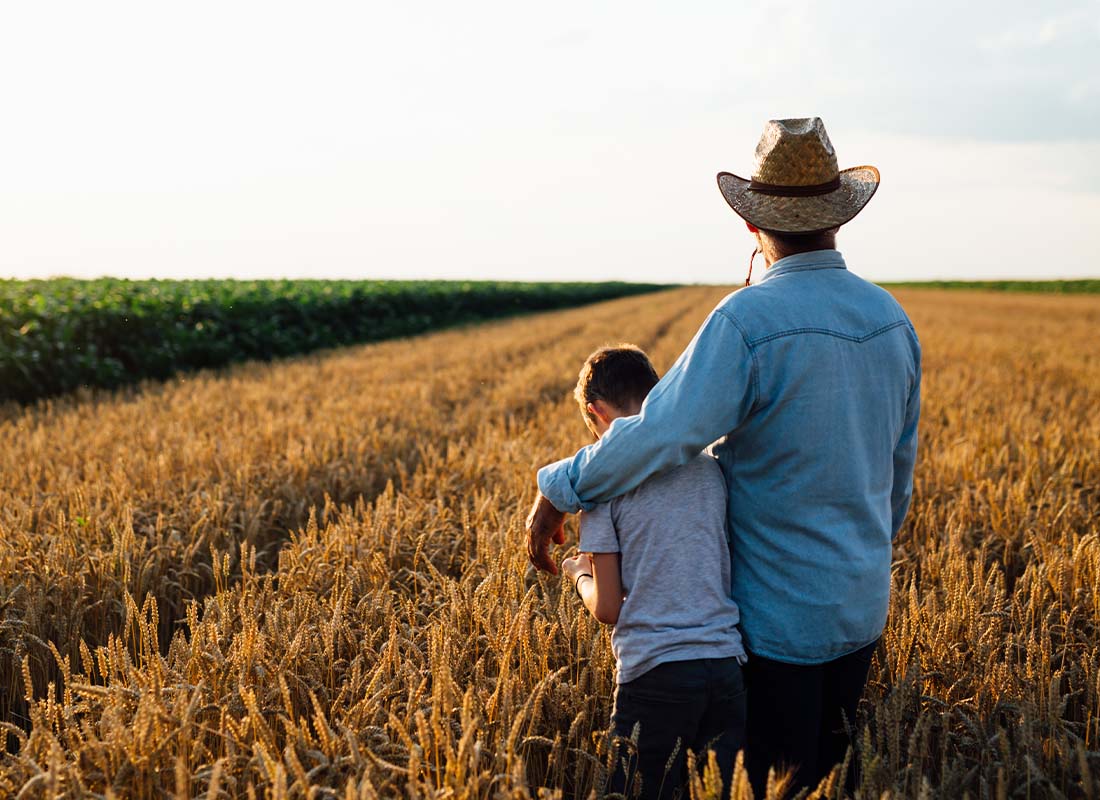 Farm and Ranch Insurance - Portrait of Farmer and His Son Walking along Their Fields of Wheat with Back Towards Camera