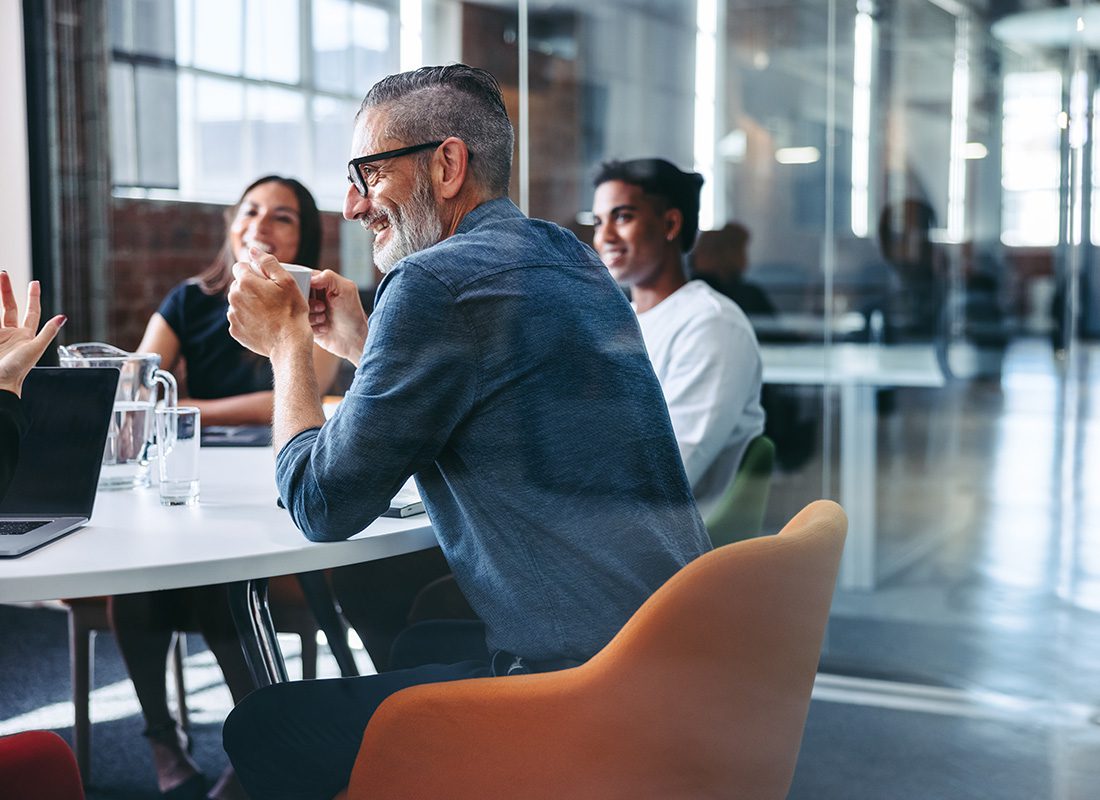 Insurance Solutions - Smiling Businessman Attending a Meeting With His Team in a Modern Office