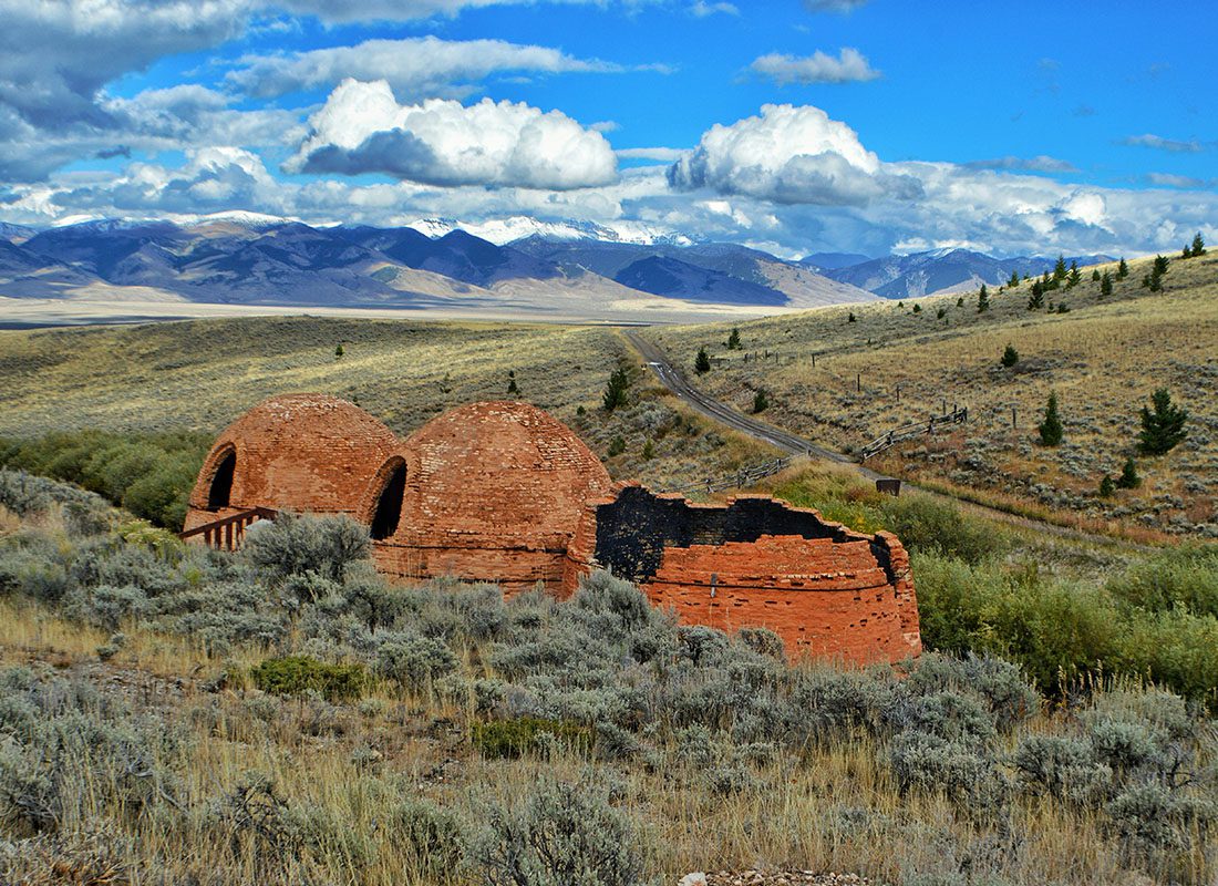 Lyman, WY - Landscape View of Birch Creek Charcoal Kilns on Grassy Field Against Sky