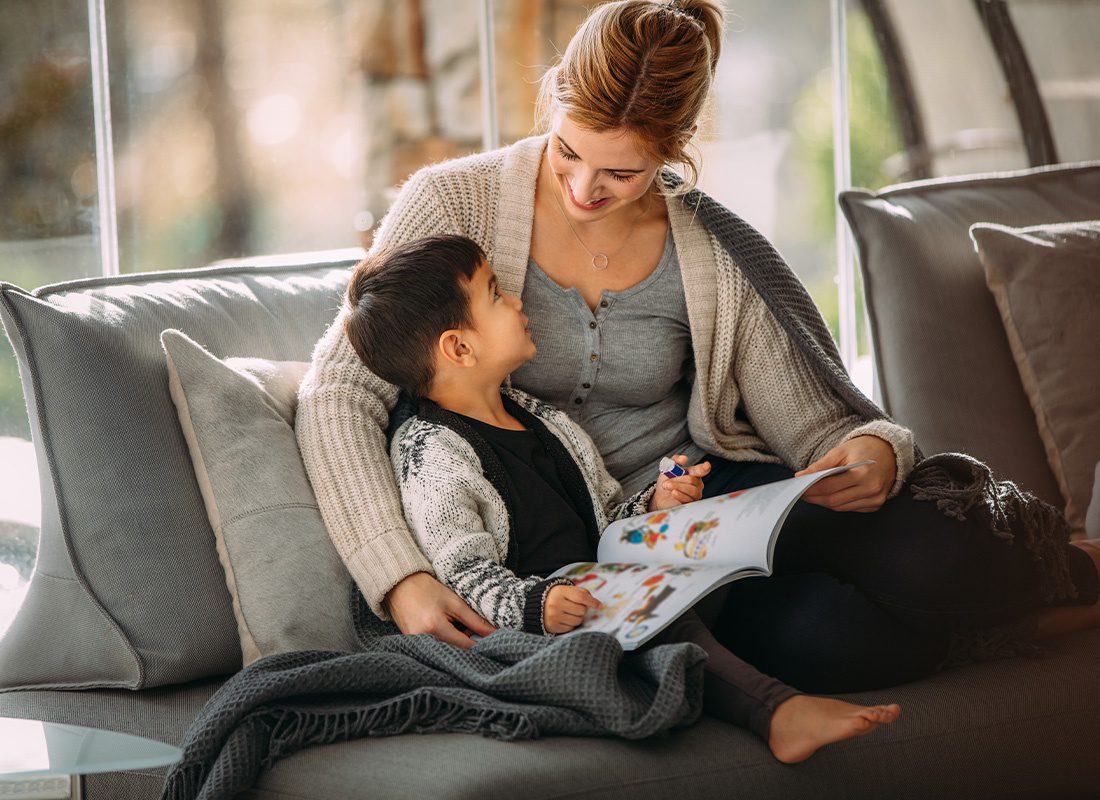 Personal Insurance - Mother and Son Reading a Story Book on the Sofa at Home