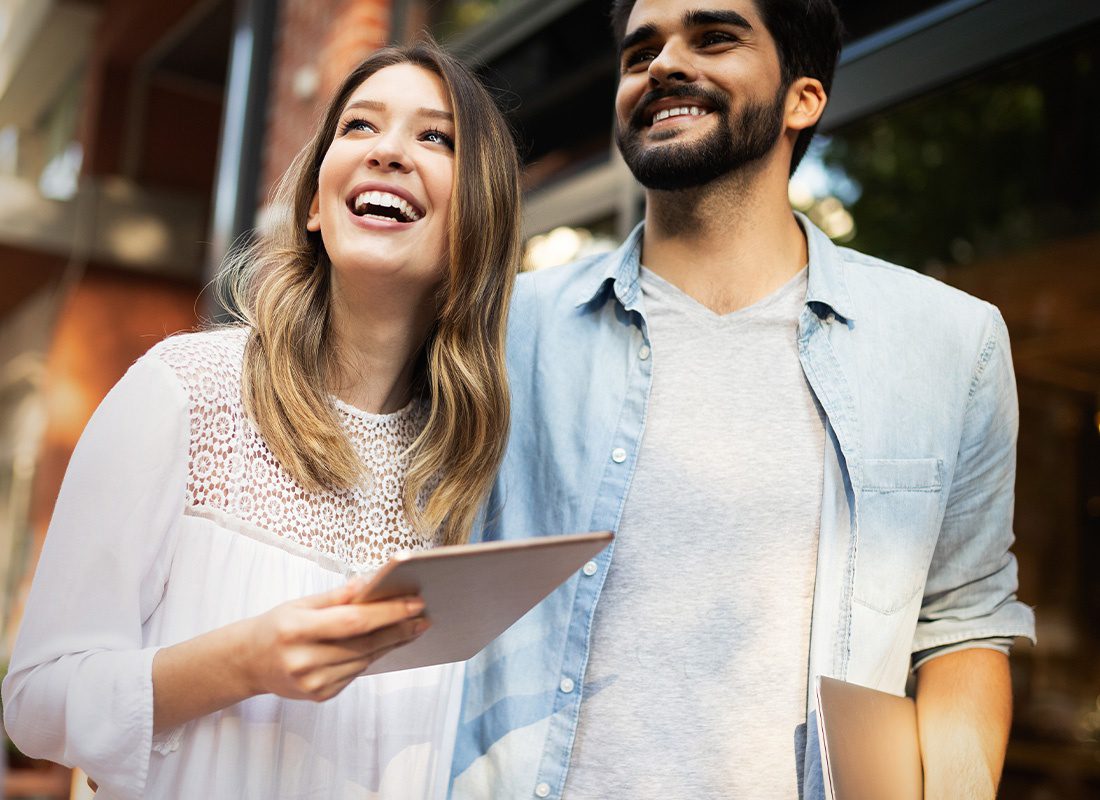 Read Our Reviews - Close Up of a Young Happy Couple Walking Outdoors with a Tablet and Looking Up on a Sunny Day